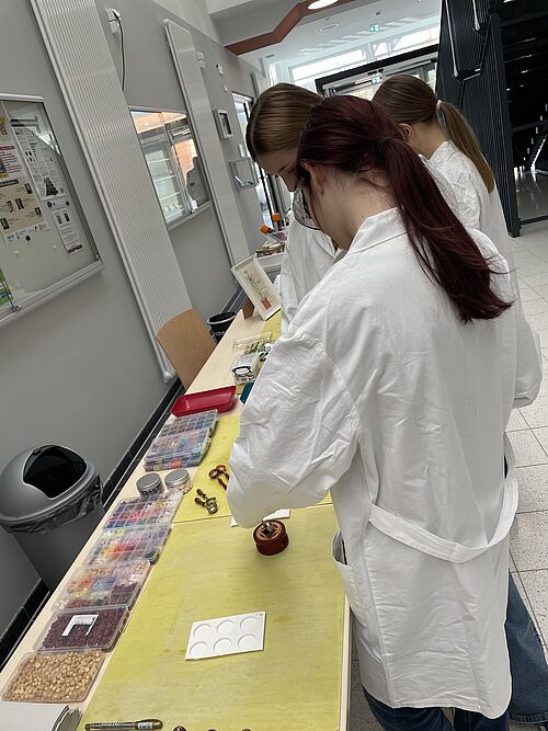 Schülerinnen in weißen Kitteln führen einfache chemische Experimente durch.