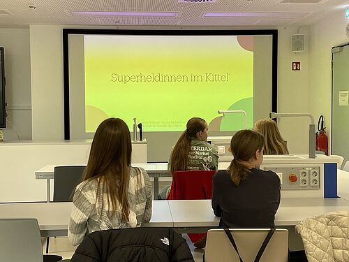 Die Schülerinnen hören einen kurzen Vortrag mit dem Titel "Superheldinnen im Kittel" in einem Seminarraum am Institut für Chemie.